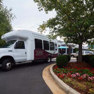 A shuttle bus parked in a lot surrounded by greenery and flowers.