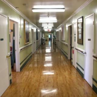 A quiet hospital corridor with multiple doors and bright overhead lighting.