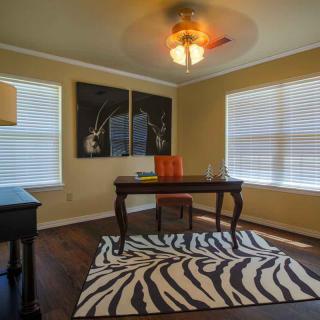 A cozy home office with a wooden desk, zebra-print rug, and large windows allowing natural light.