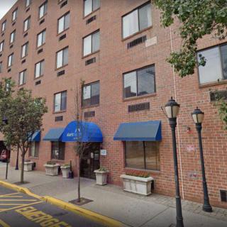 A city hotel with blue awnings on a street lined with trees and lampposts.