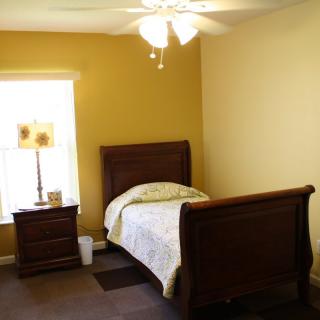 A cozy bedroom with a single wooden bed, nightstand, and a lamp near the window.