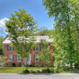 A charming brick house surrounded by lush green trees under a clear blue sky.