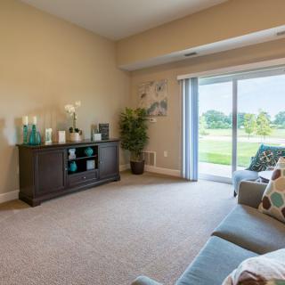 A modern living room with a sofa, TV stand, and sliding glass doors opening to a scenic view.