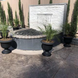 A modern garden fountain surrounded by potted plants in an outdoor setting.