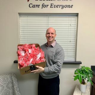A cheerful man holding a box of gifts in an office setting.