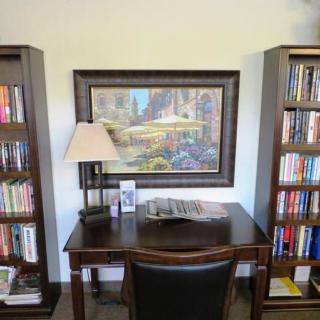 A tidy home office setup with a desk, bookshelves filled with books, and a lamp next to a decorative painting on the wall.