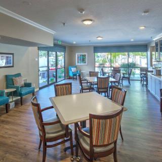 A modern dining area with tables and chairs, featuring abundant natural light and wood flooring.