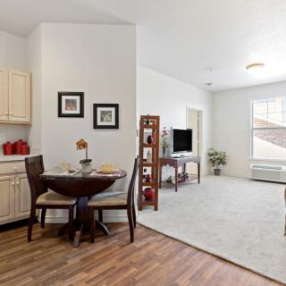 A cozy living room with an adjacent dining area and kitchenette, featuring a dining table set, a television, and tasteful decor.