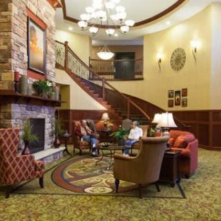 A cozy and inviting lobby featuring comfortable seating, a stone fireplace, and an elegant staircase.