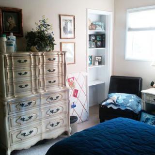 A cozy bedroom with a vintage dresser, artwork on the walls, and a comfortable chair in the corner.