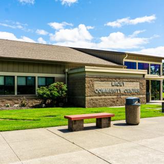 A community center building with a bench and trash can outside on a sunny day.