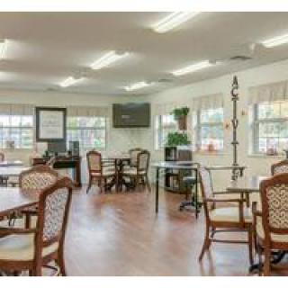 A well-lit community dining area with tables and chairs, featuring large windows and wood flooring.