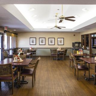 A neatly arranged dining room with wooden tables and chairs, ceiling fans, and framed artwork on the walls.