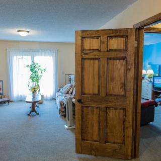 A cozy living room with wooden door, furniture, and a potted plant by the window.
