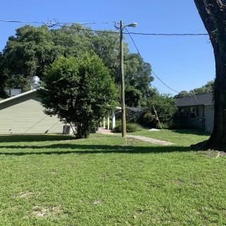 A sunny suburban scene with a house and a grassy yard surrounded by trees.