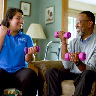 A caregiver and an elderly man engaging in a light exercise session using dumbbells, promoting health and wellness.