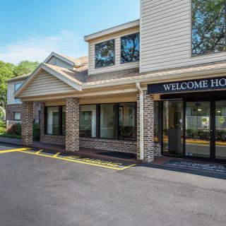 The entrance of a hotel building with a 'Welcome Home' sign on a sunny day.