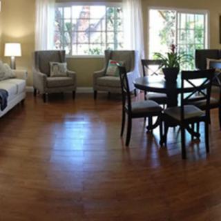 A cozy living room with hardwood floors and modern furniture, including a sofa, chairs, and a dining table near large windows.