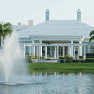 A picturesque view of a large building with white columns, surrounded by palm trees and a fountain in the foreground.