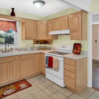 A cozy kitchen featuring wooden cabinets, a stove with oven, and a tiled floor.