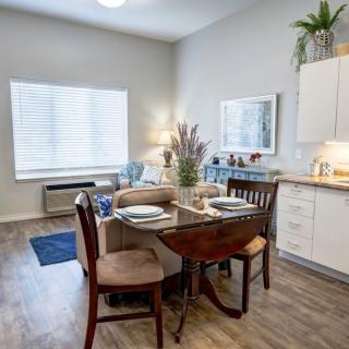 A cozy dining area with a wooden table set for two, adjacent to a compact kitchen.