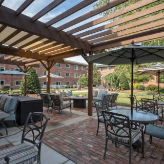 A tranquil outdoor patio area featuring tables, chairs, and a pergola with views of a garden.