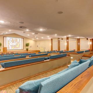 A spacious auditorium with rows of seating and a projector screen at the front.