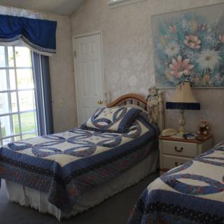 A cozy bedroom with twin beds covered in blue and white quilts, complemented by a floral painting and classic decor.