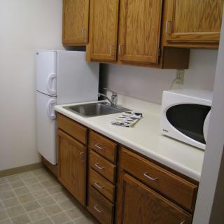 A compact apartment kitchen with wooden cabinets, a refrigerator, microwave, and sink.