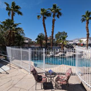 A sunny outdoor area featuring a swimming pool surrounded by palm trees and patio furniture.