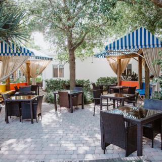 A charming outdoor cafe area featuring tables and chairs under striped canopies, surrounded by trees and greenery.
