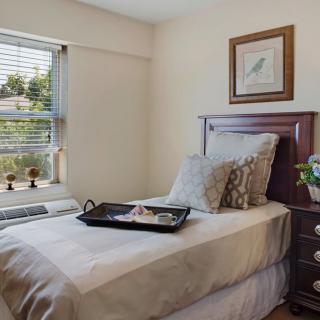 A cozy single bedroom with a neatly arranged bed, decorated with pillows and a small tray. Natural daylight filters through the window, adding warmth to the room.