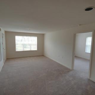 An empty room with carpet flooring and ample natural light coming through a window.