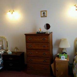 A cozy bedroom featuring a central wooden dresser, flanked by nightstands with lamps and wall-mounted lights.