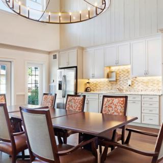 A modern kitchen and dining area featuring a large wooden table, comfortable chairs, white cabinets, and a stylish chandelier.