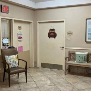 A cozy waiting room with chairs and decorative pillows, featuring signs and a closed door.