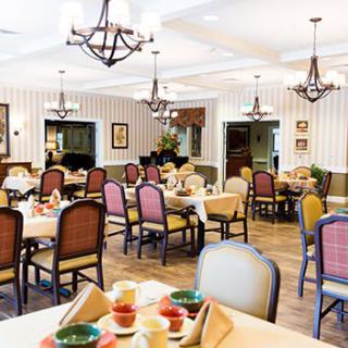 A well-decorated dining room with multiple tables and chairs, featuring chandeliers and a cozy atmosphere.