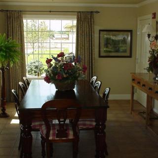A cozy dining room with a wooden table and chairs, adorned with floral decorations and greenery near a large window.