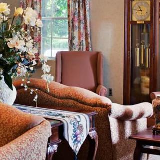 A cozy living room with a sofa, grandfather clock, and floral decorations.