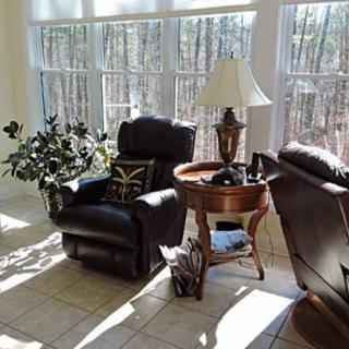 A cozy living room area with two chairs, a lamp on a side table, and sunlight streaming through large windows.