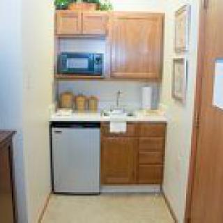 A compact kitchen area with a microwave, cabinets, mini refrigerator, and sink.
