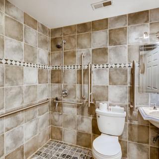 An accessible bathroom with tiled walls and floor, featuring a toilet, sink, and grab bars.