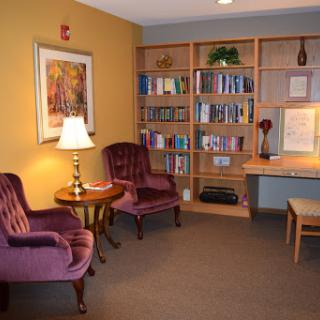 A cozy reading nook featuring two velvet chairs, a warm lamp, and a bookshelf filled with various books.