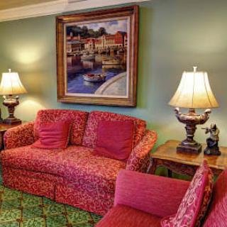 A cozy living room with a red patterned sofa, elegant lamps, and a painting on the wall.