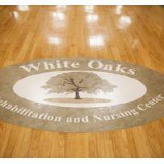 Logo of White Oaks Rehabilitation and Nursing Center on a wooden floor.