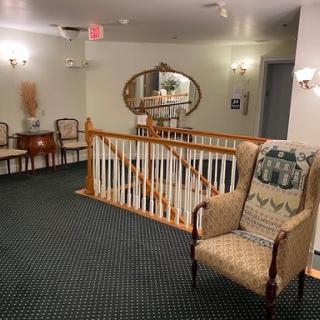 A cozy hallway with traditional decor, featuring an armchair, mirror, and wood railing.