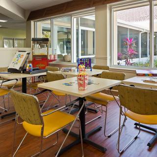 A cozy dining area with tables and chairs, featuring a popcorn machine and large windows.