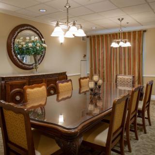An elegant dining room with a long table, surrounded by chairs and adorned with a chandelier.