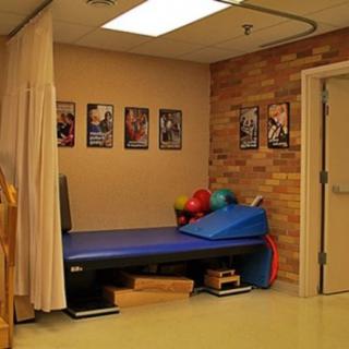 A physical therapy treatment room with a mat, exercise balls, and motivational posters on the wall.