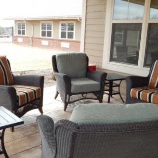 A cozy outdoor patio area with cushioned chairs and a table, set against the backdrop of a building.